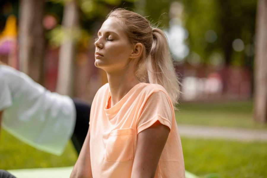 Young slender girl with closing eyes doing yoga exercises on the yoga mat on green grass in the park on a warm day. Yoga on the open air .